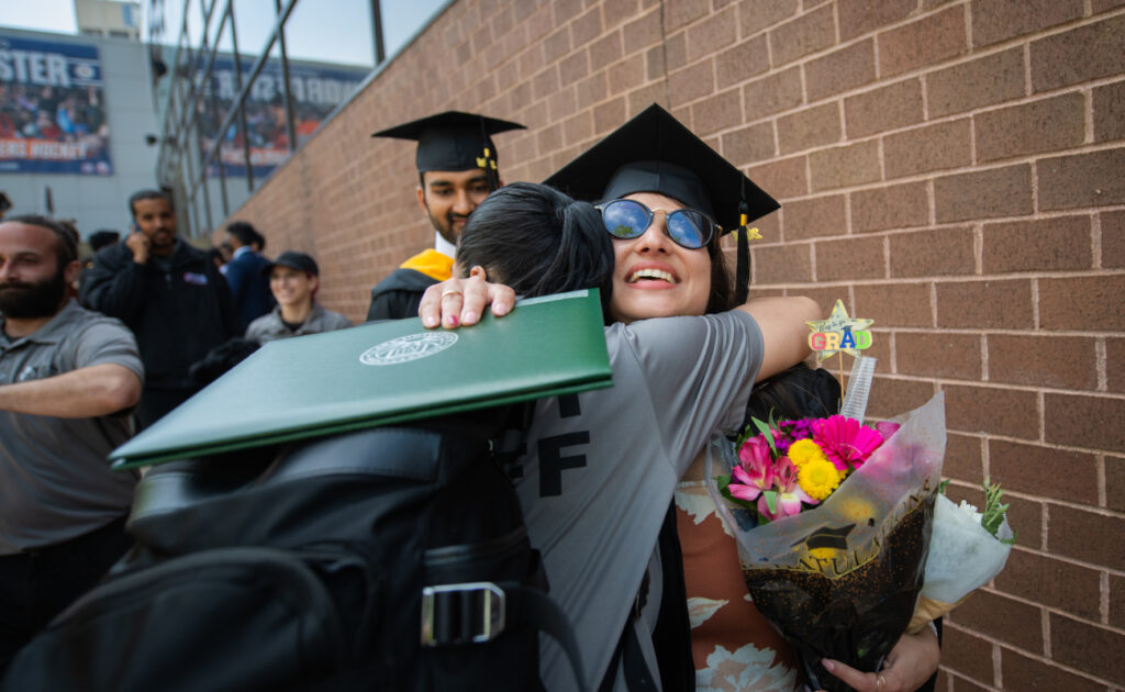 Students hugging with diploma in hand