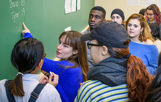Students in Clark classroom crowded around professor pointing to blackboard