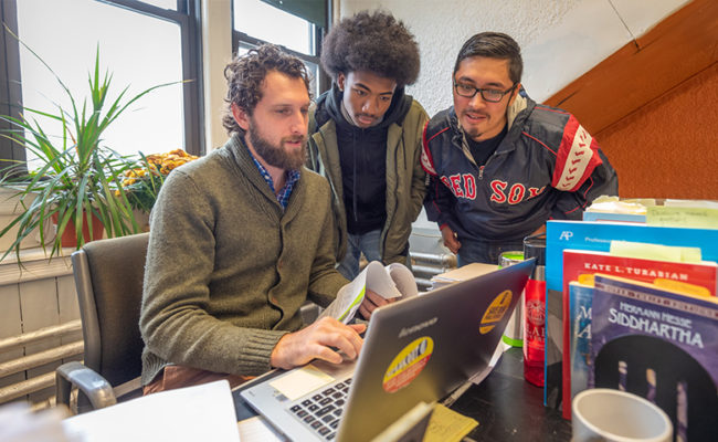 Male teacher showing two young male high school students something on computer