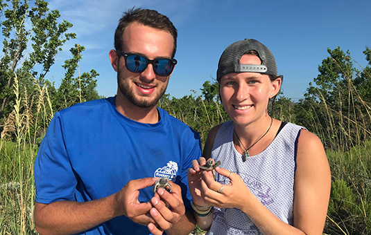 two students holding baby turtles