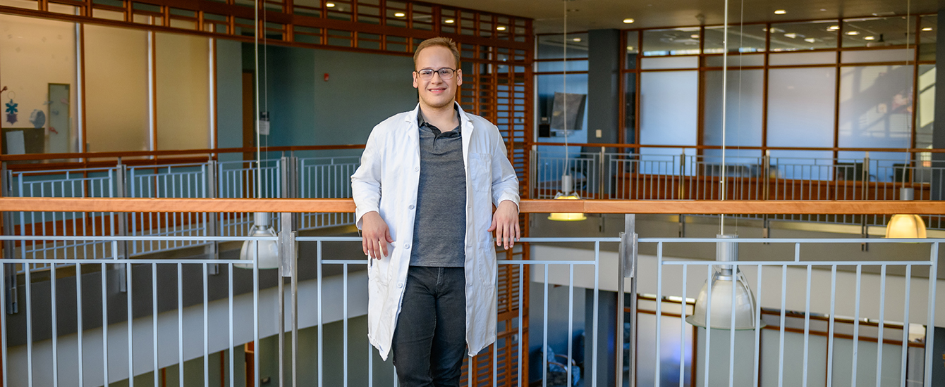 student with white coat on leaning on railing