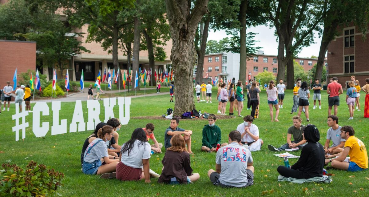 students sit in circle on campus green next to #CLARKU letter
