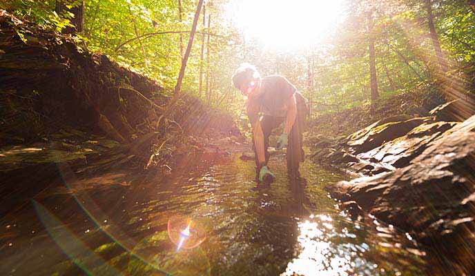 a student takes a water sample from a creek bed