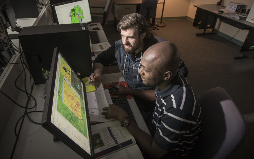 two students looking over geographic maps on computers