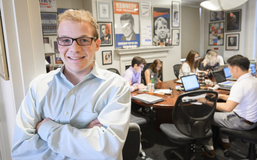 Political science student in conferene room with other students with political posters behind them