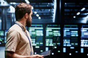 A person on a laptop stands beside a supercomputer