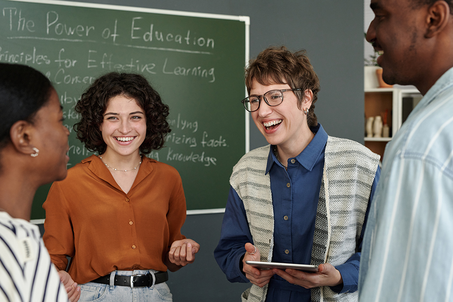 Group of people discussing principles for effective learning in a classroom setting with a chalkboard in background. Group members are smiling and engaged in conversation