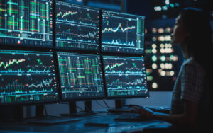 Finance Student looking over 6 computer monitors with analytics