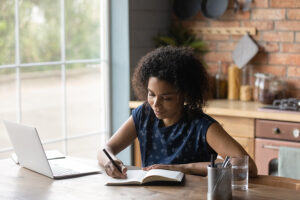 publishing & literary journals: female writing in book with laptop