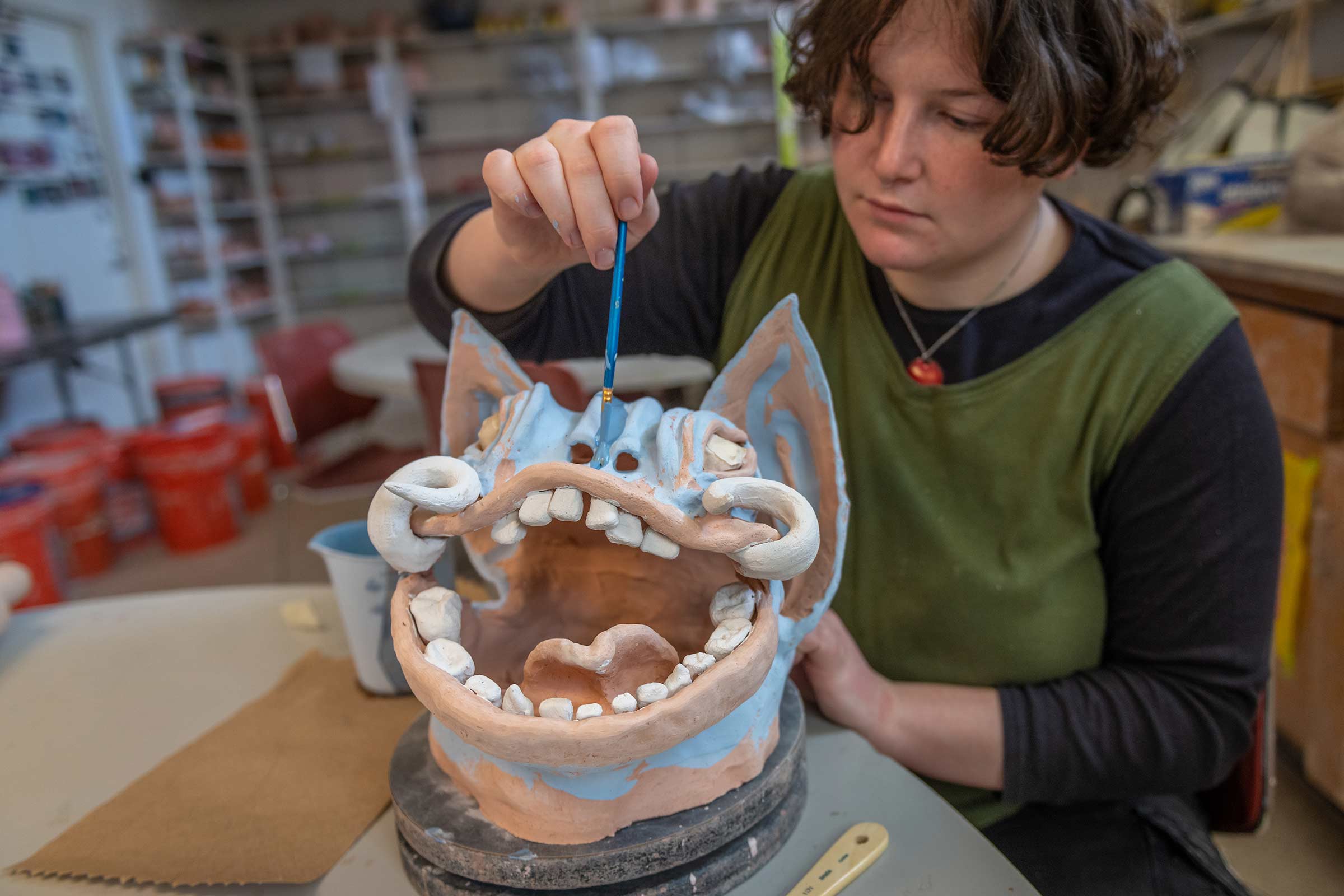 Brynn Kevin glazing a clay sculpture of a dragon