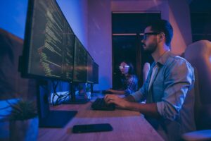 Two people seated before large monitors working on coding projects