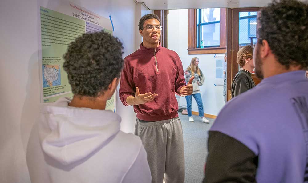 Aedan Derrick ’26, center and Matt Shea ’26, left, present their research project, “Climate Change Adaptations of Major American Waterways,” at the poster salon that culminated their first-year intensive course.