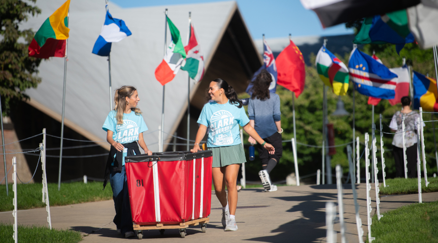 Two girls pushing moving bin through Clark campus