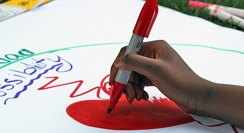A student teacher works on a large educational sign with the word 'possibility partially visible.