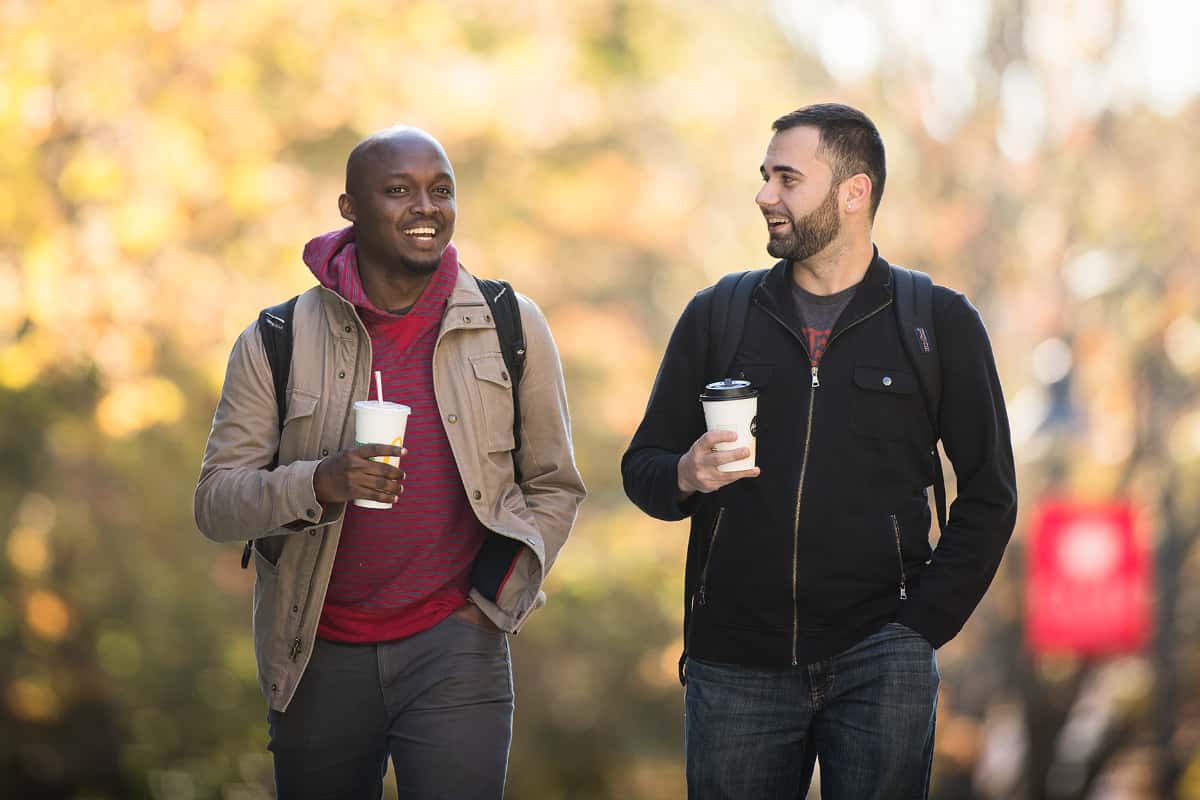Graduate students walking down path carrying coffee