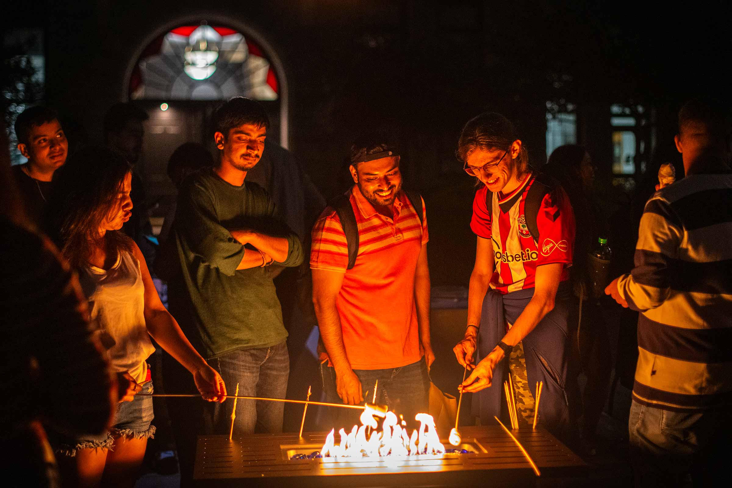 Students toast marshmallows at night during one of the Saturday evening activities